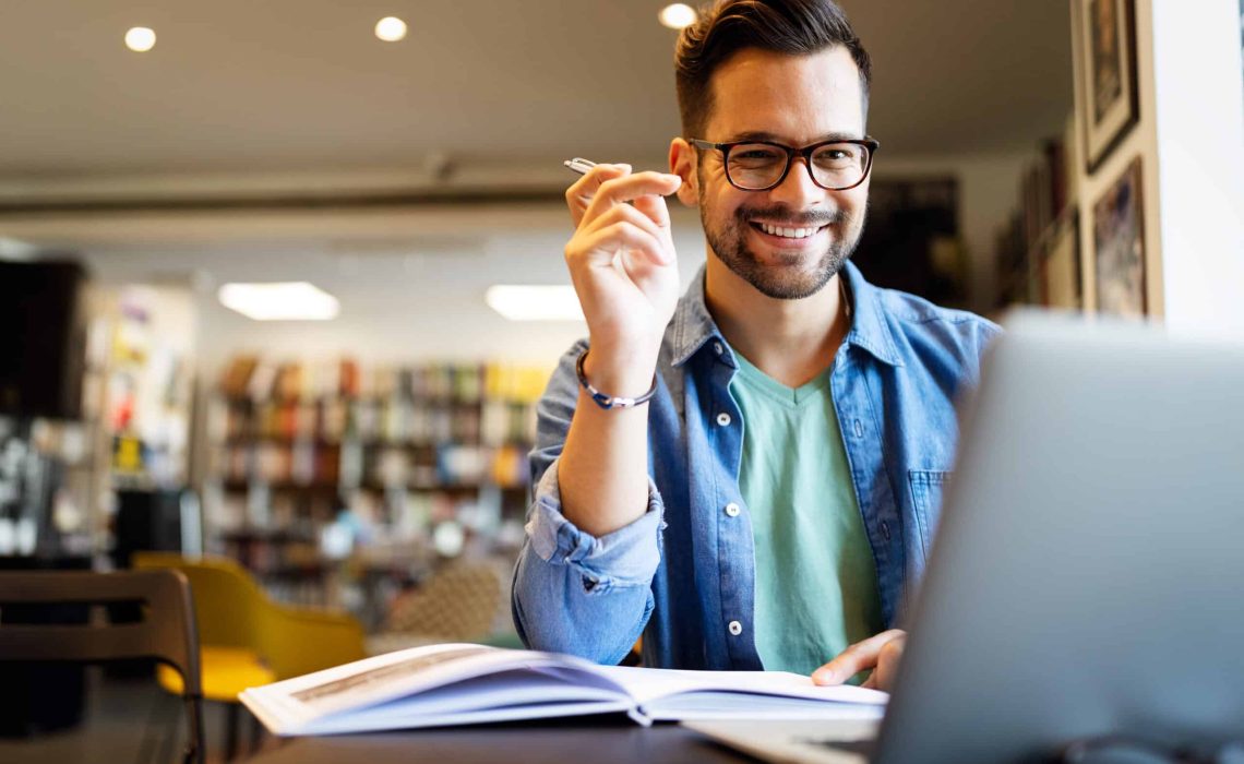 Smiling male student working and learning in a library